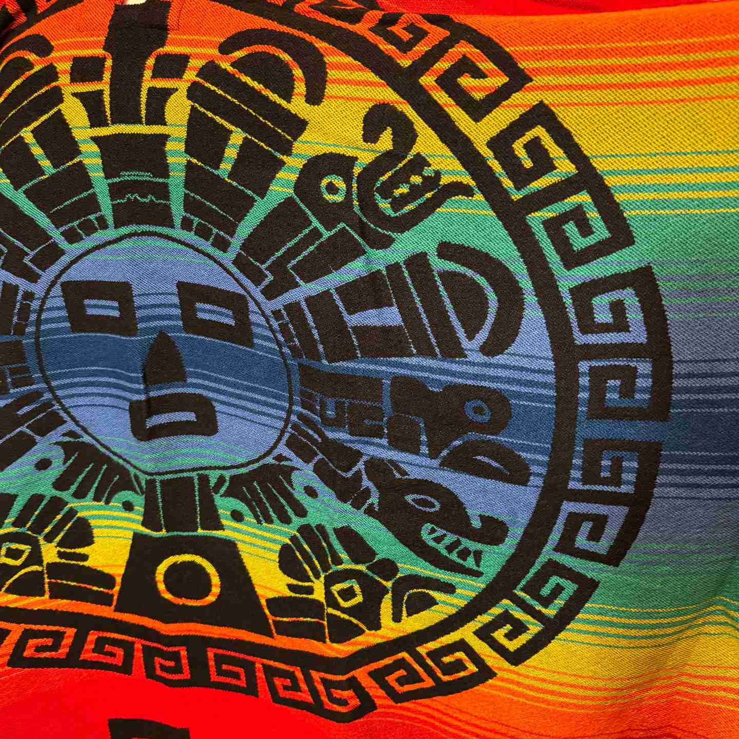 Close-up of circular sun face medallion with rainbow gradient on Sunstone Spectrum Crimson poncho